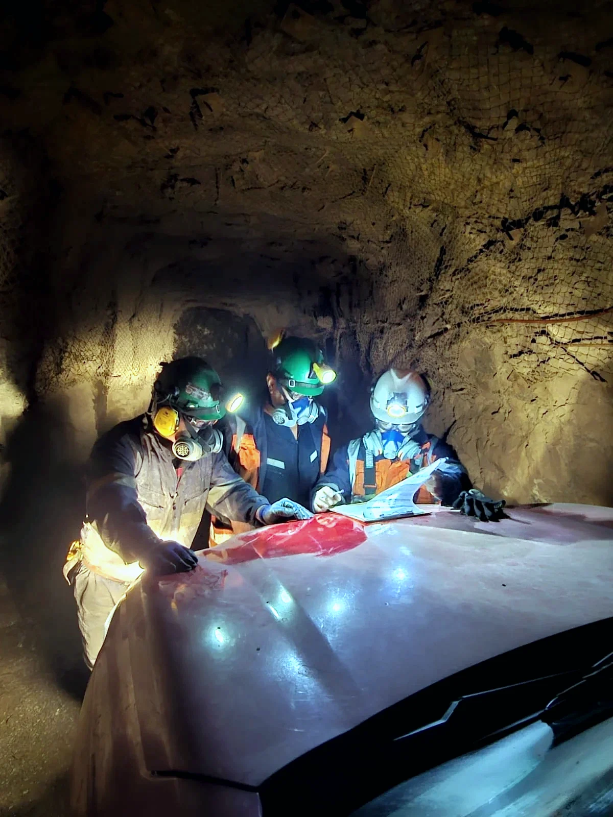 Equipo de trabajadores mineros revisando documentos en una labor subterránea